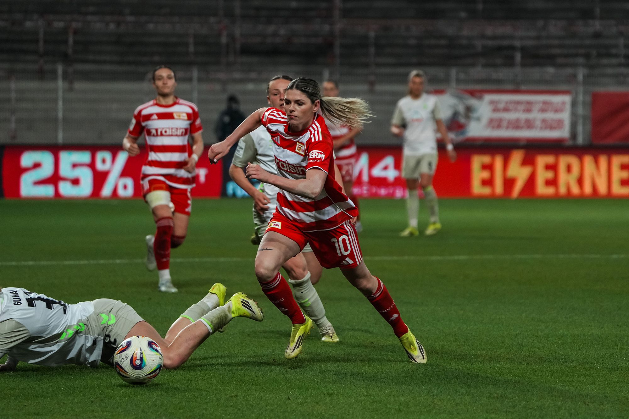Spielszene im Frauenfußball: Eine Spielerin in Rot dribbelt, während eine Gegnerin am Boden liegt.