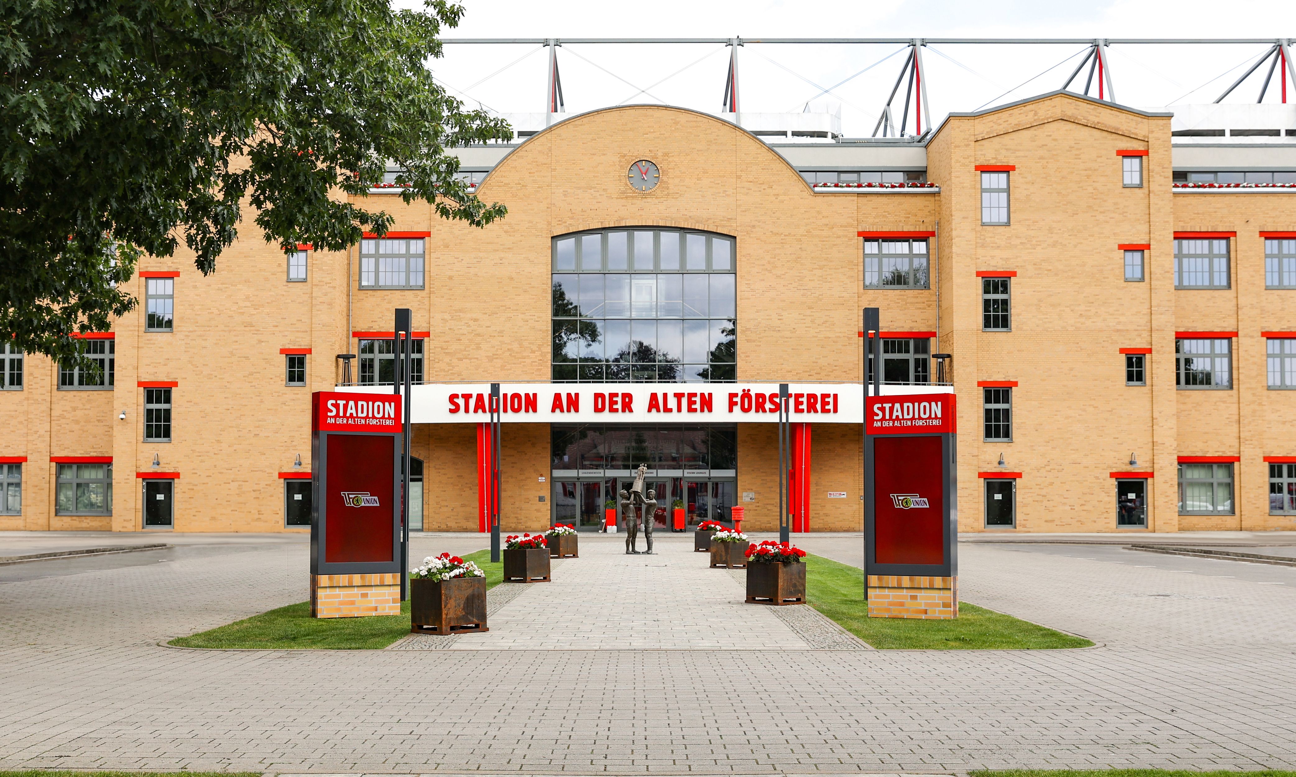 Stadion an der Alten Försterei mit rotem und gelbem Mauerwerk, Eingangstor und dekorativen Blumenarrangements.