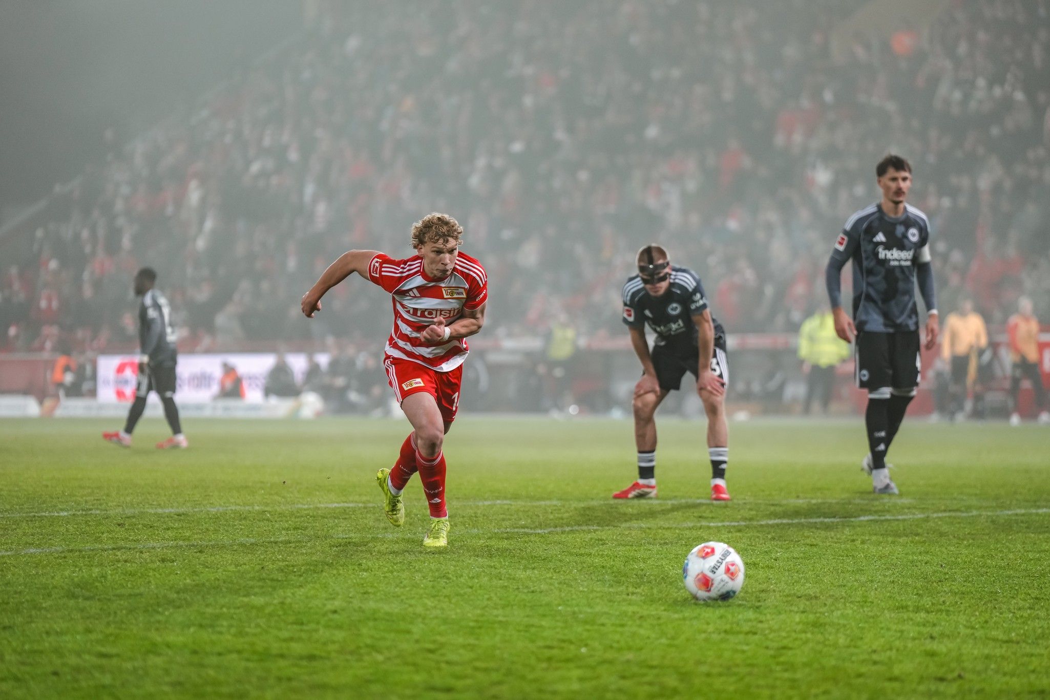 Ein Fußballspieler sprintet auf den Ball zu, während zwei Gegner in Torwartuniform auf den Elfmeterpunkt warten.