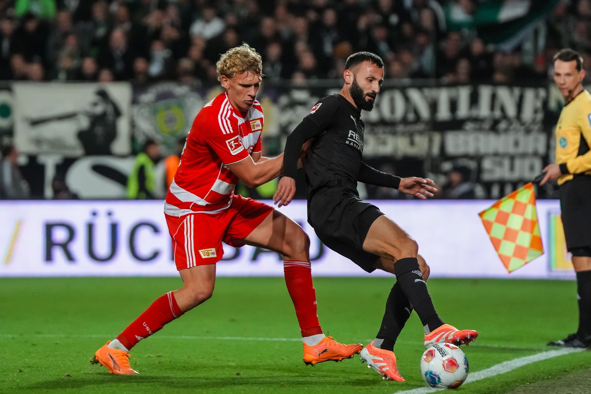 Spielszene zwischen zwei Fußballspielern, einer in rot-weißer und der andere in schwarzer Uniform, im Wettkampf um den Ball.