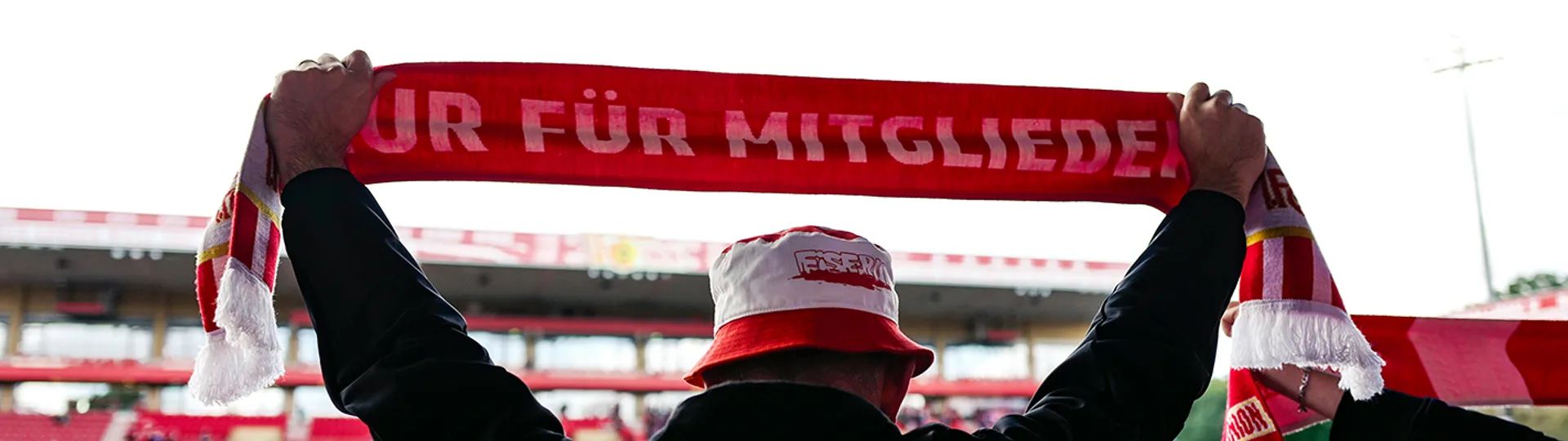 A large crowd in a stadium holds up red and white scarves while cheering for their team.