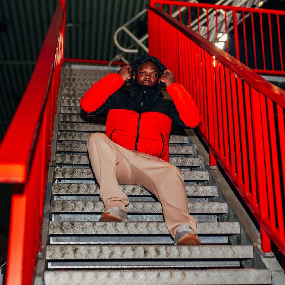 Person in rotem und schwarzem Outfit sitzt auf einer metallischen Treppe mit rotem Geländer.