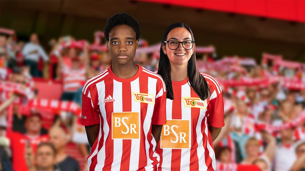 Two people in red and white striped jerseys are smiling in front of a crowd in a stadium.