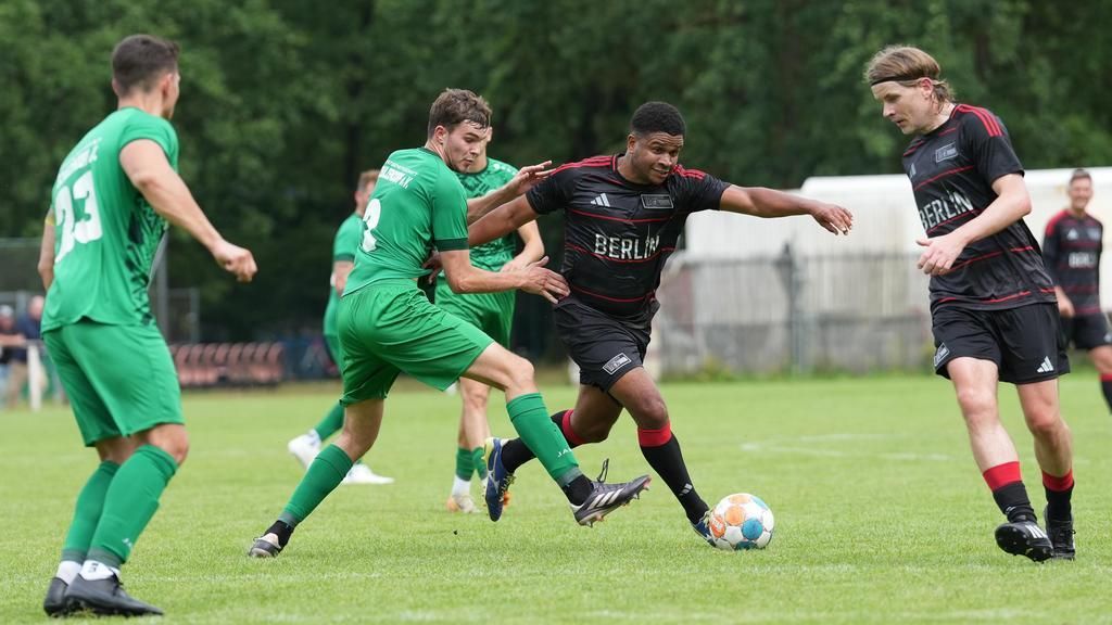 Zwei Fußballteams im Spiel: Ein Spieler in Schwarz dribbelt den Ball, während zwei Spieler in Grün ihn versuchen zu stoppen.