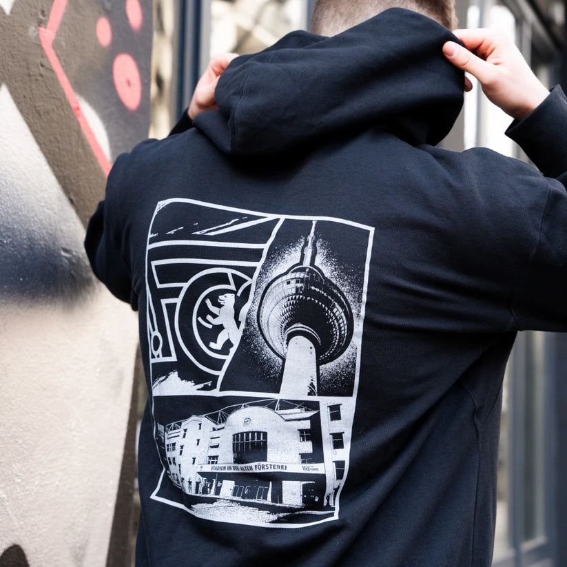 Mann von hinten in einem schwarzen Hoodie mit grafischem Print, der eine Darstellung des Fernsehturms und eines Gebäudes zeigt.