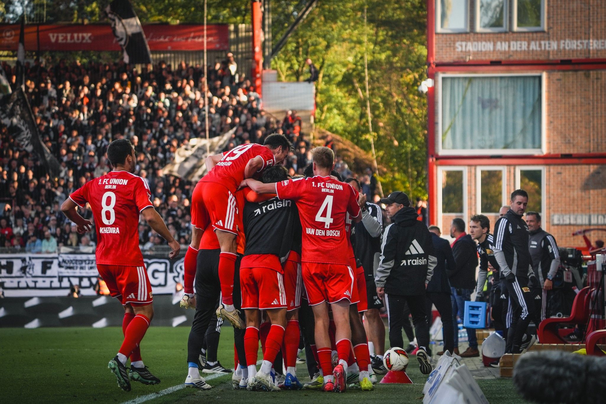 Spieler des 1. FC Union Berlin umarmen sich nach einem Tor, während die Zuschauer im Hintergrund jubeln.