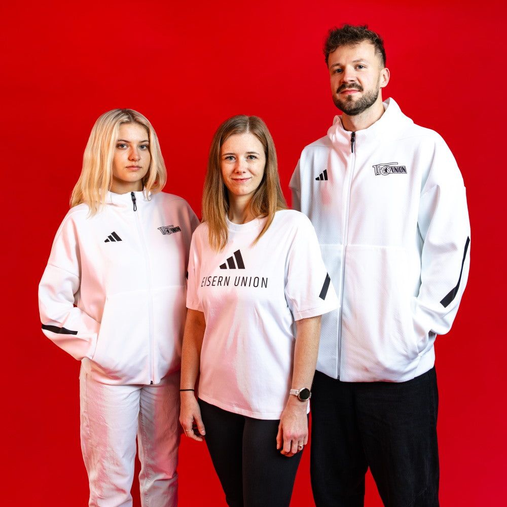 Drei Personen stehen vor einem roten Hintergrund, gekleidet in weiße Sportbekleidung mit dem Logo von Eiserner Union.