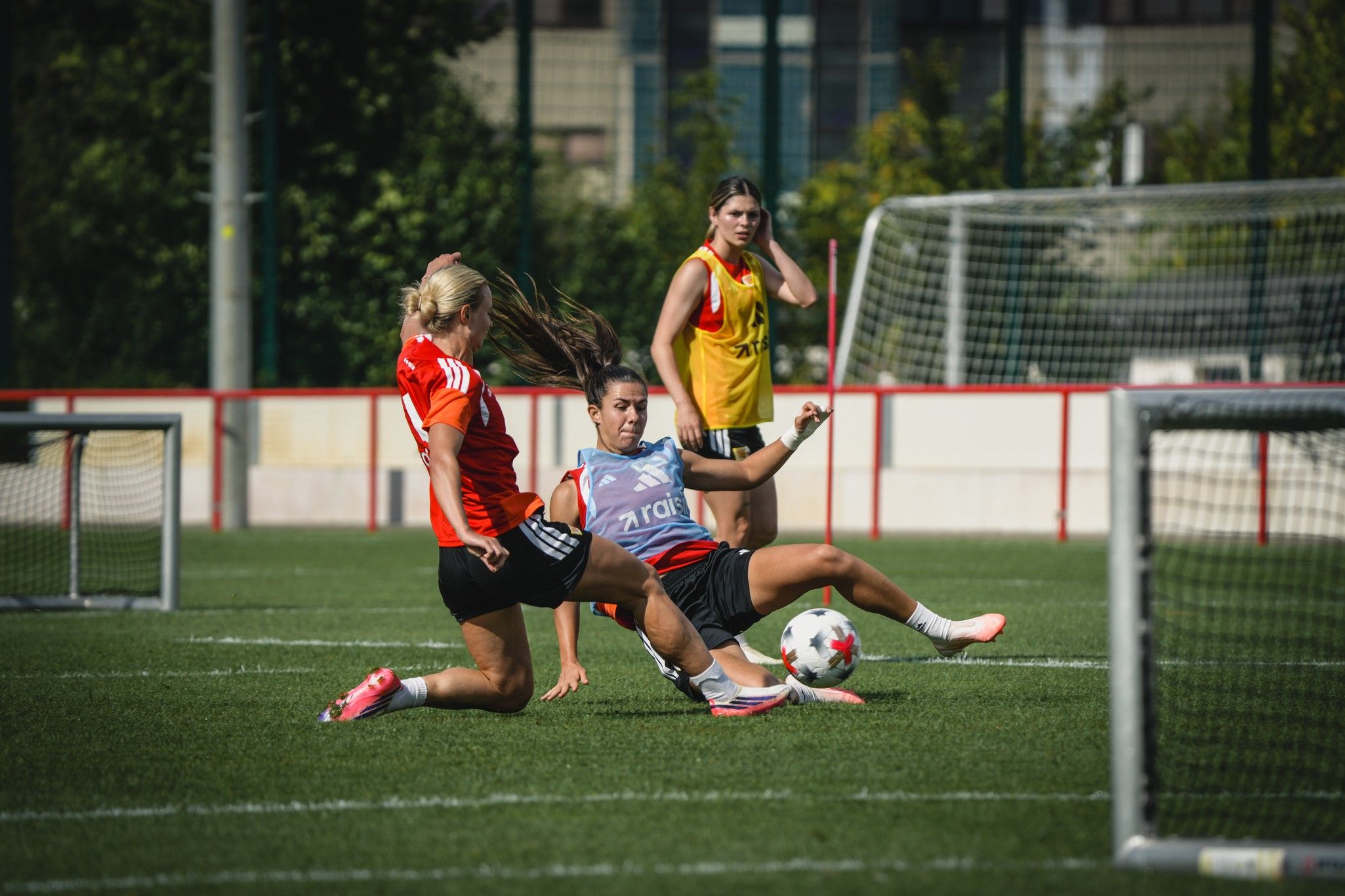 Drei Fußballspielerinnen trainieren auf einem Spielfeld, während eine Spielerin einen Tackling-Versuch unternimmt.