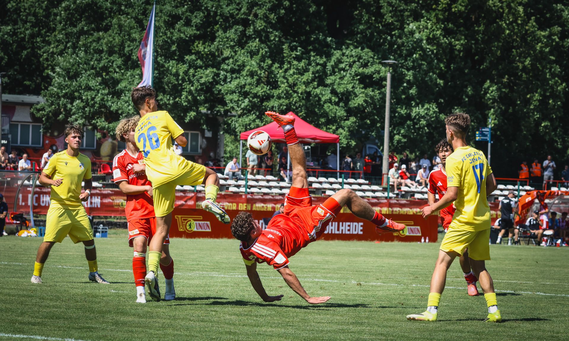 Ein Fußballspieler führt einen akrobatischen Rückwärtssalto aus, während andere Spieler um ihn herum stehen und zuschauen.