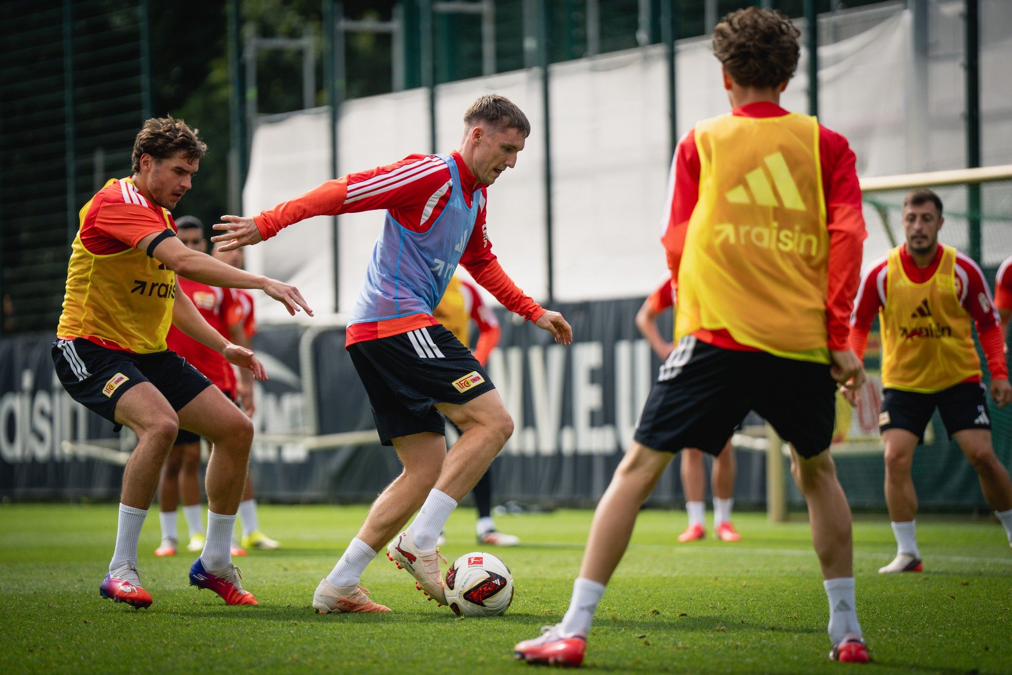 Spieler in einem Fußballtraining dribbeln den Ball auf einem Rasenplatz, umgeben von Mitspielern.