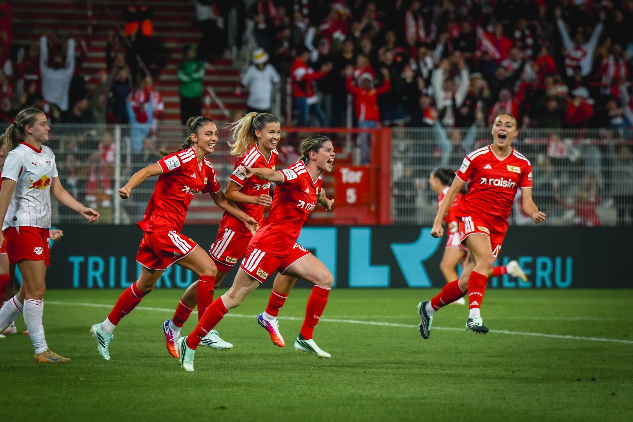 Spielerinnen von Union Berlin feiern ein Tor während eines Fußballspiels, im Hintergrund jubelnde Fans.