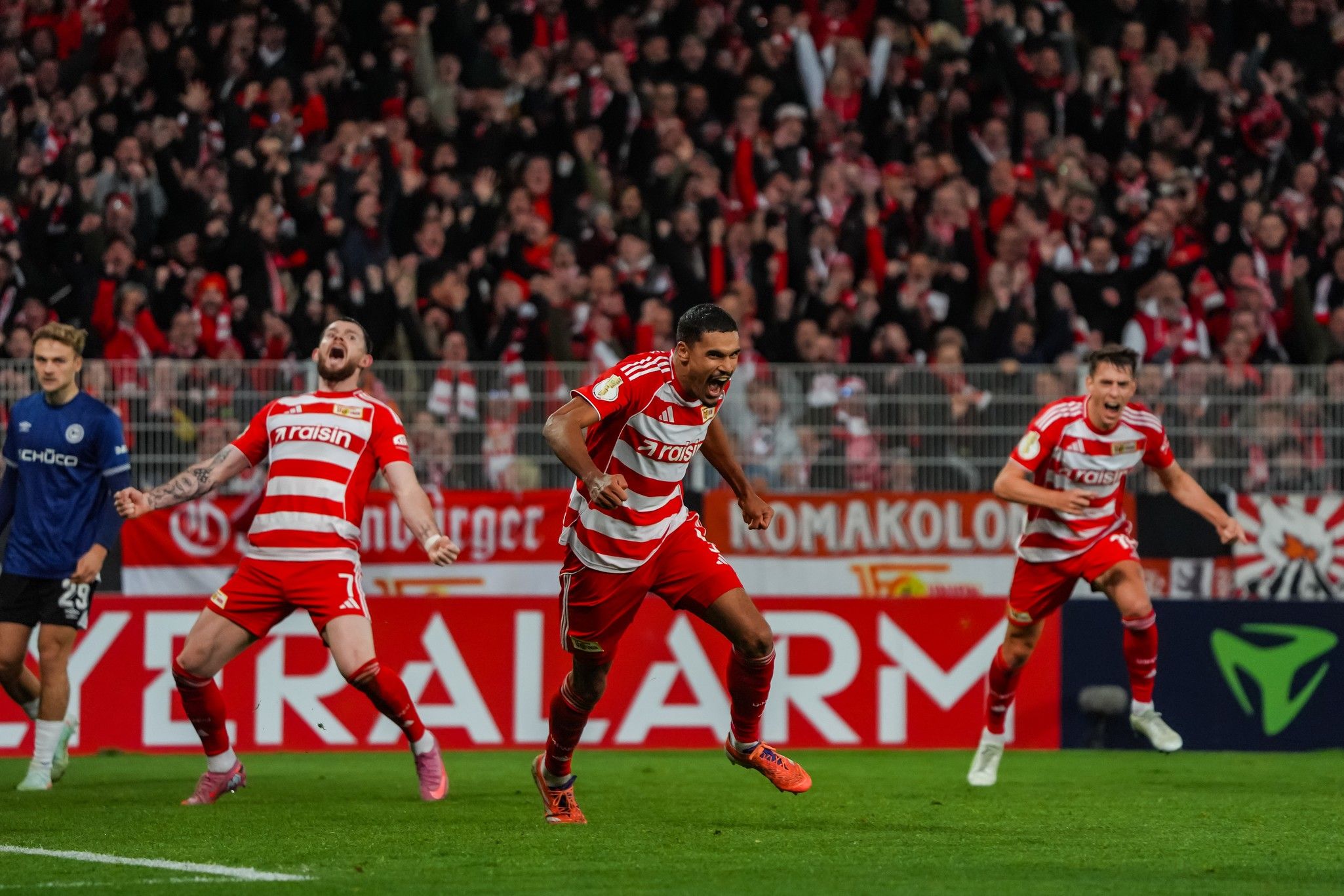 Fußballspieler jubeln nach einem Tor in einem Stadion voller fans, gekleidet in rot-gestreifte Trikots.