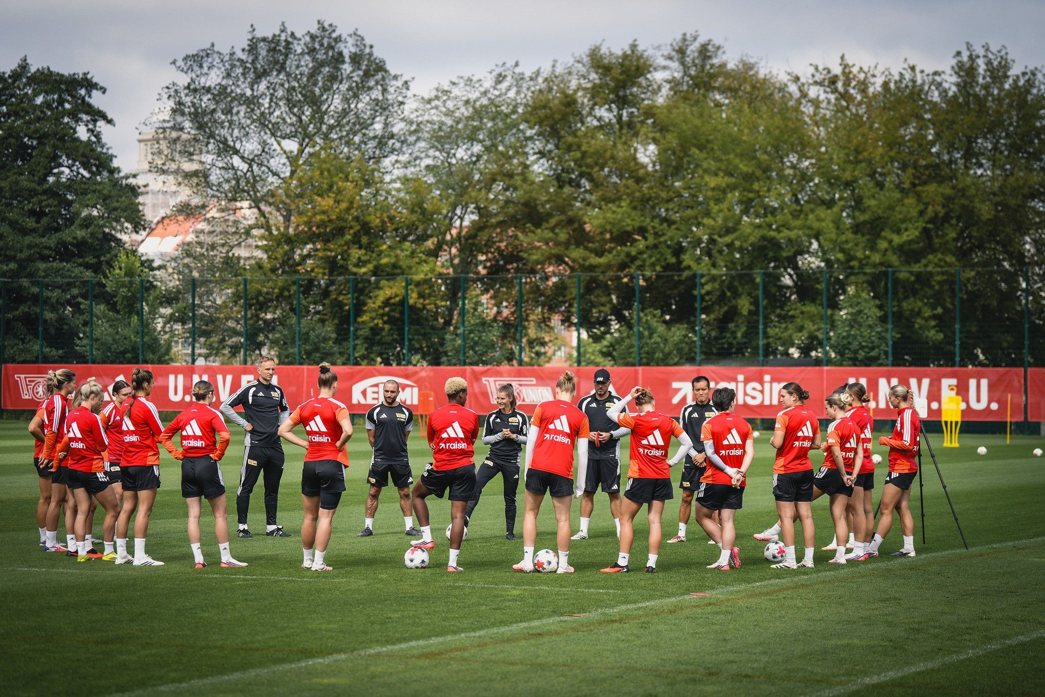 Eine Gruppe von Fußballspielern in roten Trainingsanzügen versammelt sich auf dem Platz zur Besprechung während des Trainings.