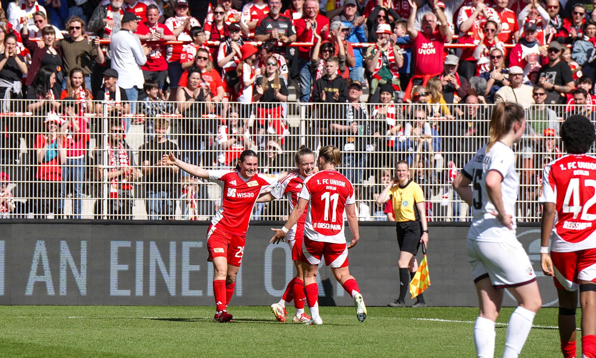 Fußballspielerinnen feiern ein Tor vor jubelndem Publikum in einem Stadion.