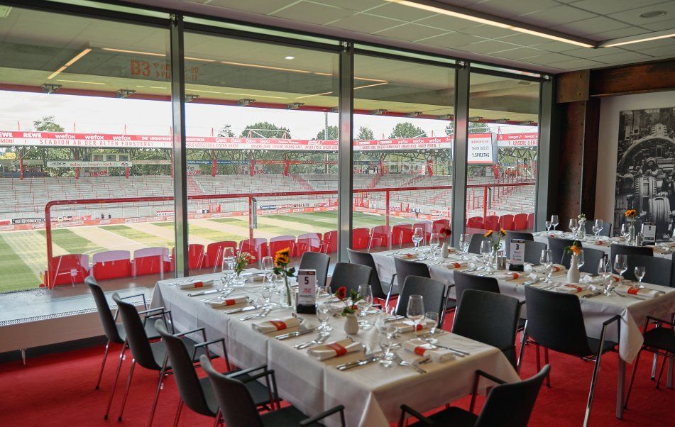 Ein elegantes Restaurant mit gedeckten Tischen und Blick auf ein Fußballfeld durch große Fenster.