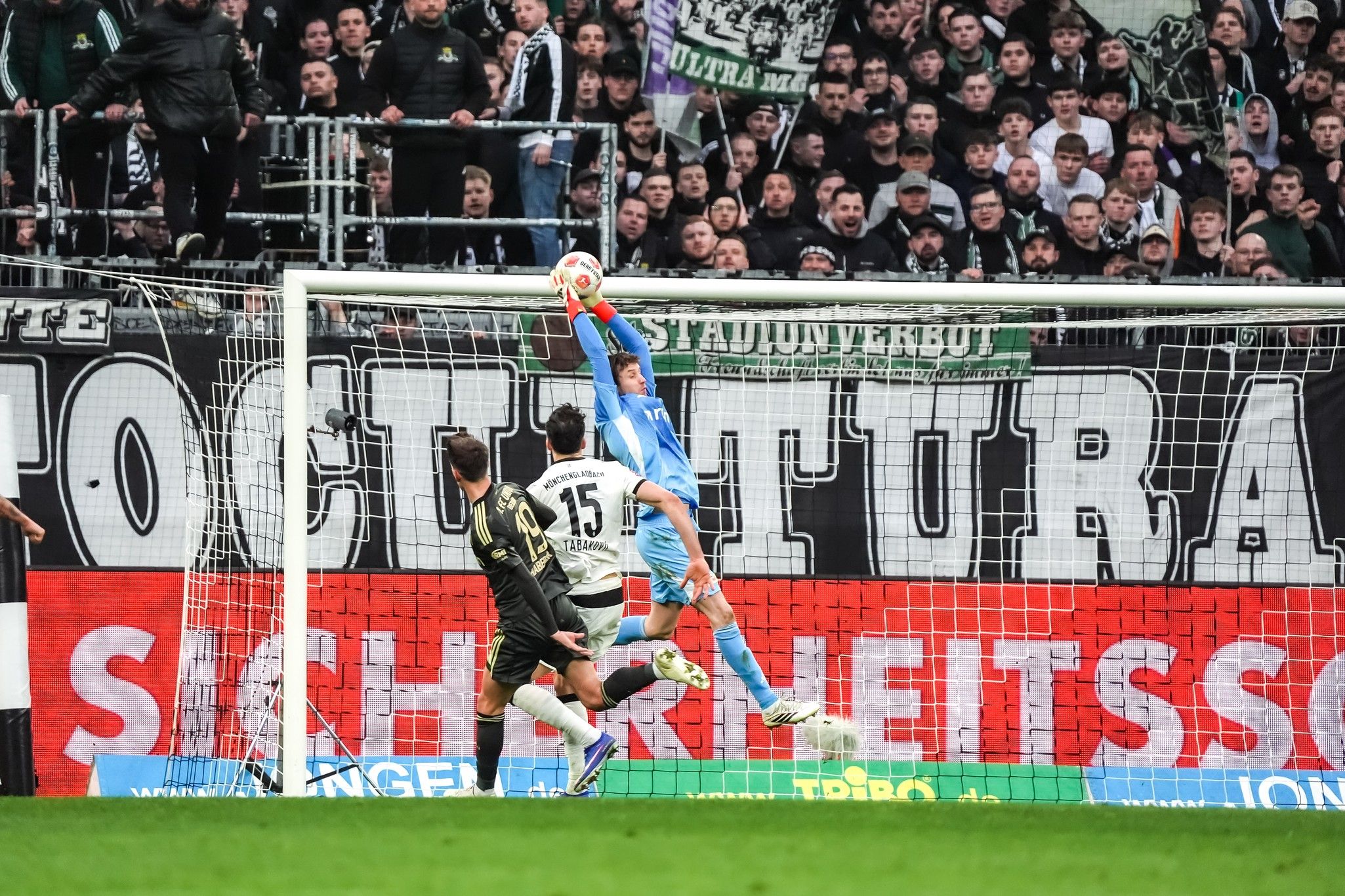 Torhüter greift nach dem Ball in einem Fußballspiel vor einer jubelnden Menge.