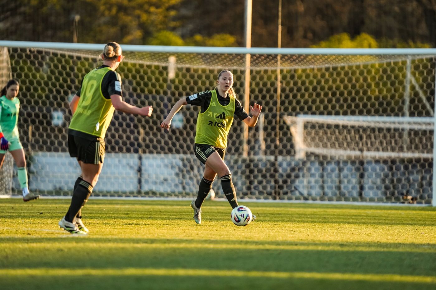 Zwei Fußballspielerinnen auf dem Platz, eine dribbelt den Ball, die andere bereitet sich auf einen Pass vor.