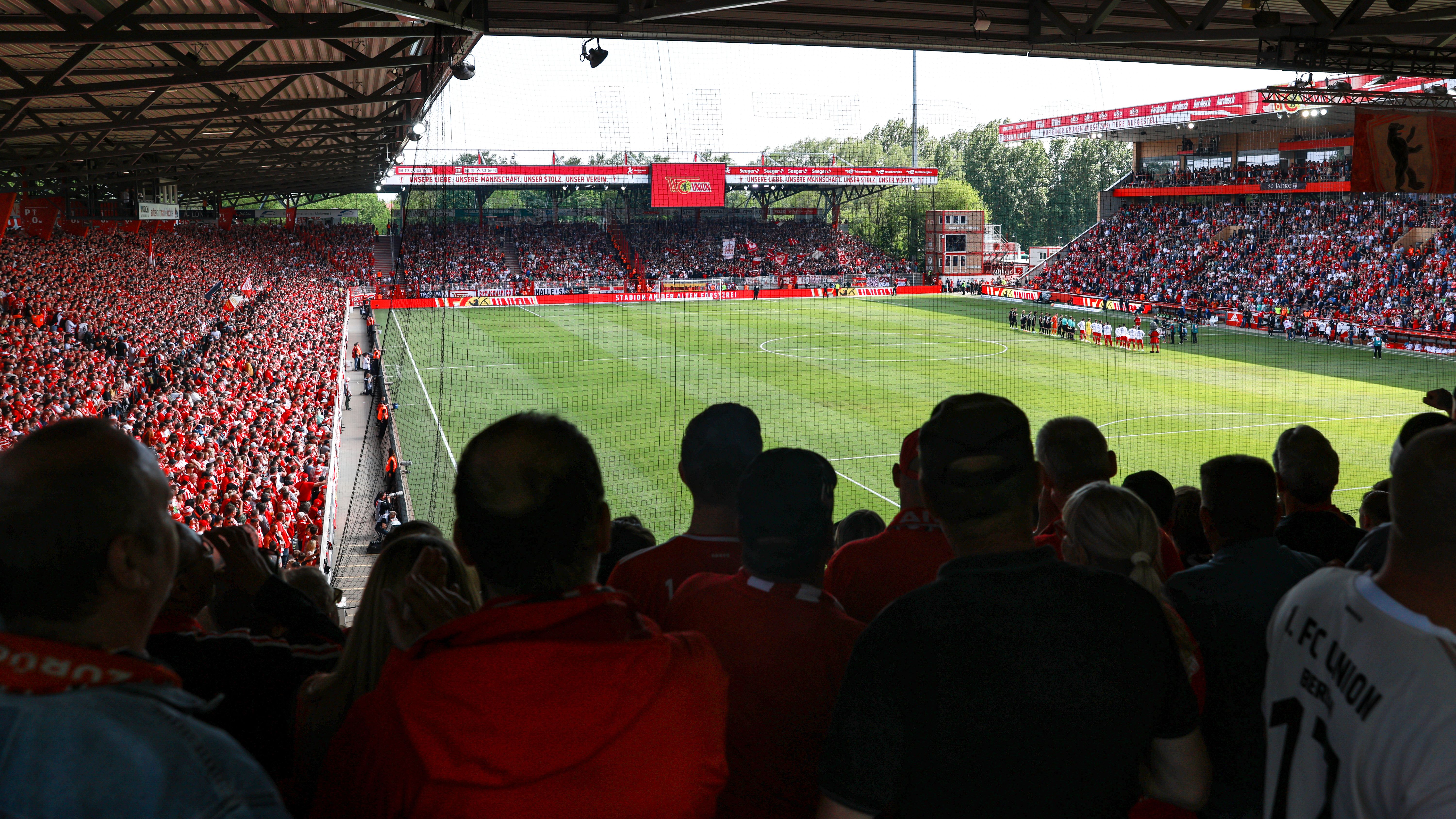 Volle Stadionränge mit Fans in roten Trikots, Blick auf den Spielfeldrand vor dem Spielbeginn.