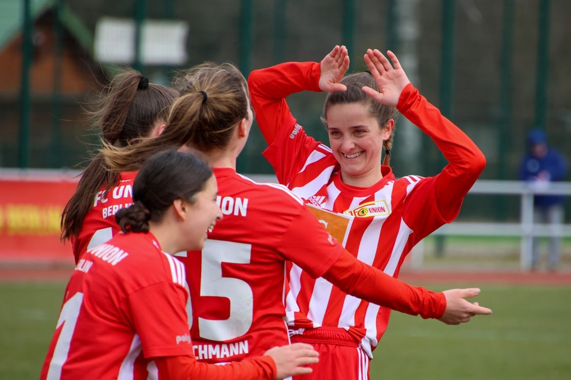 Spielerinnen des FC Union feiern einen Torerfolg auf dem Fußballfeld, begleitet von Freude und Teamgeist.