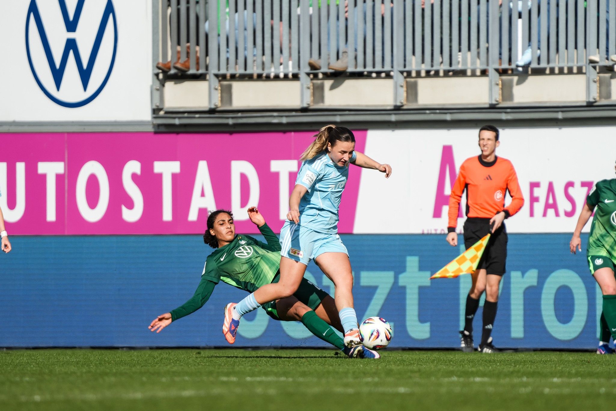 Eine Spielerin in hellblauem Trikot wird von einer Spielerin in grünem Trikot im Fußballspiel zu Boden gerissen.