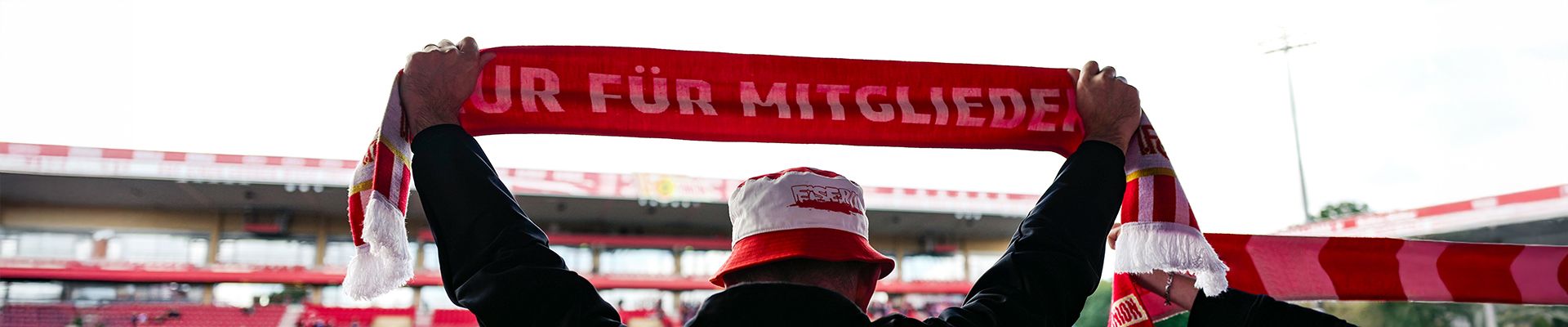 Ein Fan hält einen roten Schal mit der Aufschrift "Für Mitglieder" in einem Stadion hoch.