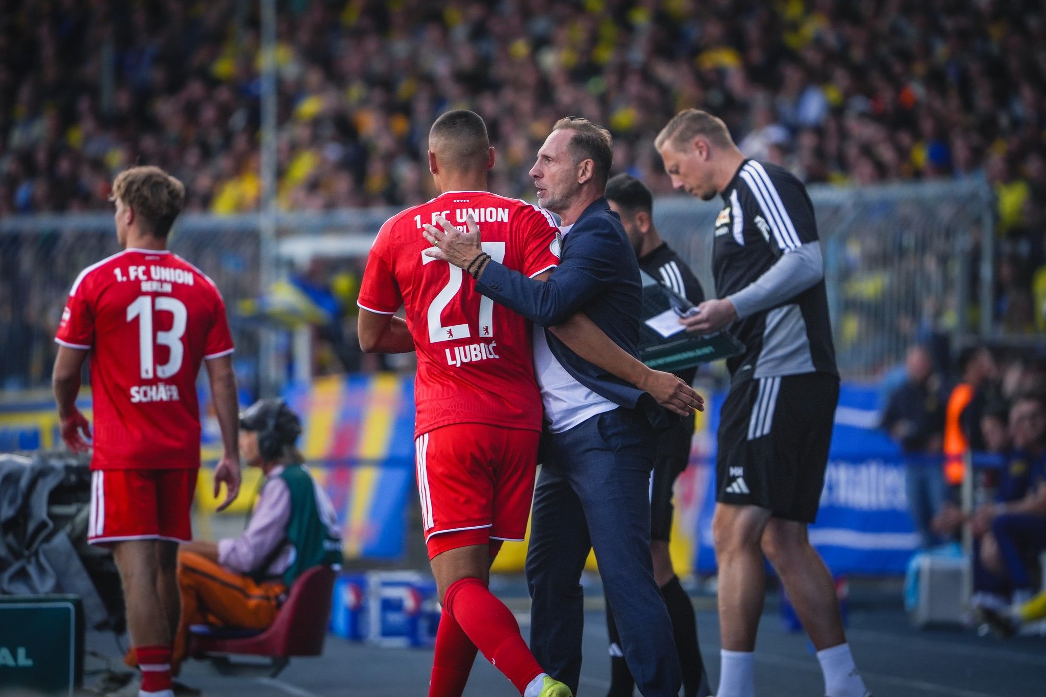 Ein Trainer spricht mit einem Spieler der Mannschaft 1. FC Union, während andere Spieler und Staff im Hintergrund stehen.
