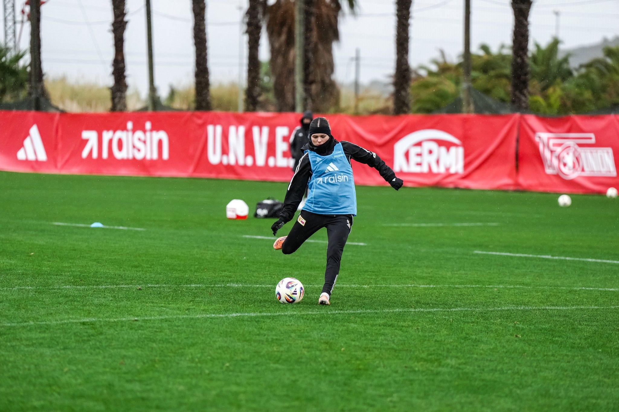 Eine Fußballspielerin in Trainingskleidung tritt einen Ball auf einem grünen Platz während eines Trainings.