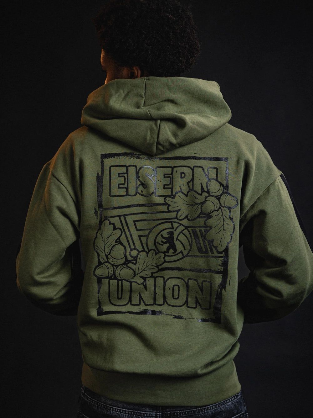 Person trägt einen olivgrünen Hoodie mit einem schwarzen Aufdruck, der den Schriftzug "EISERN UNION" und Eichenblätter zeigt.