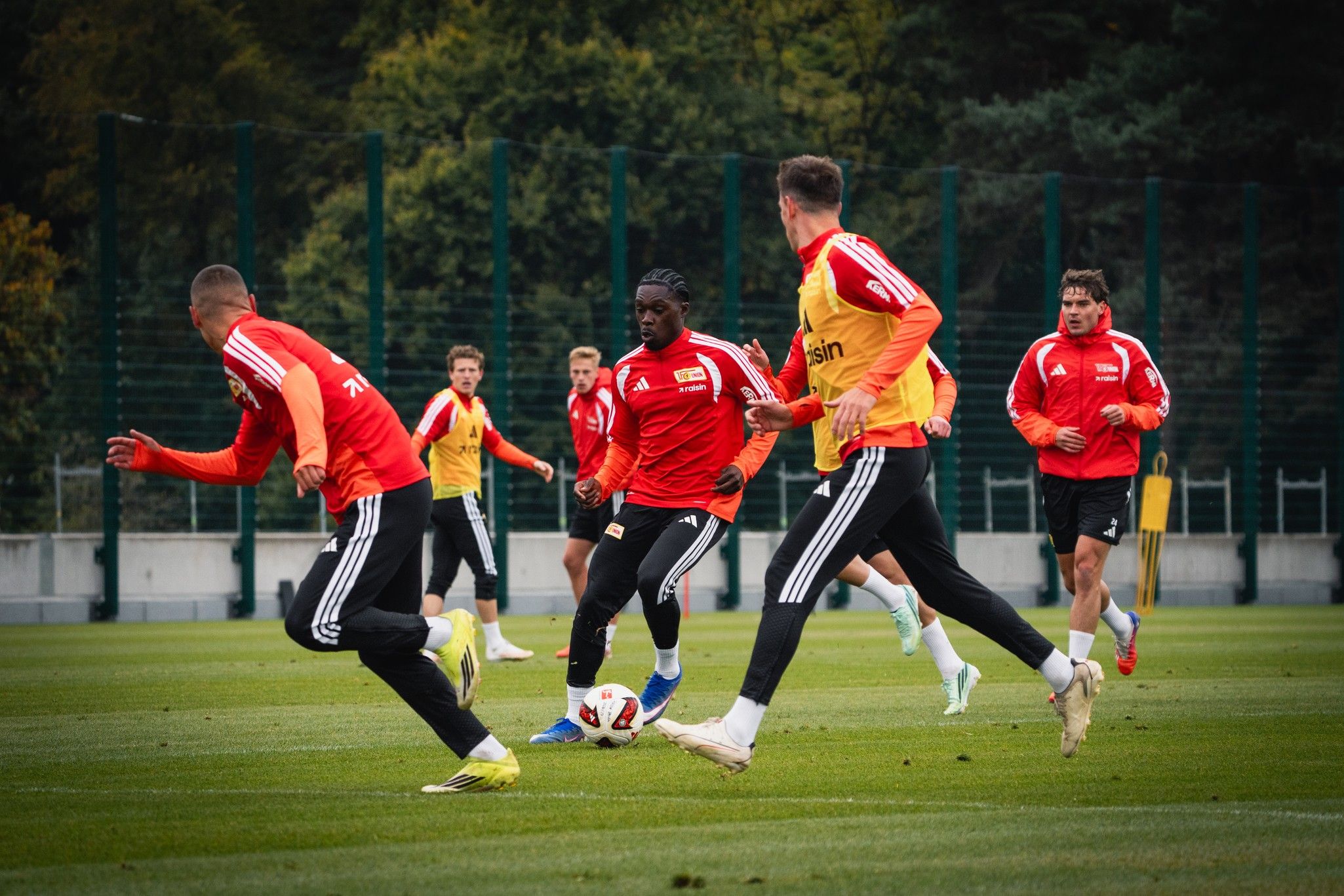 Fußballmannschaft beim Training auf dem Platz, Spieler in roten und gelben Trikots dribbeln und passen den Ball.