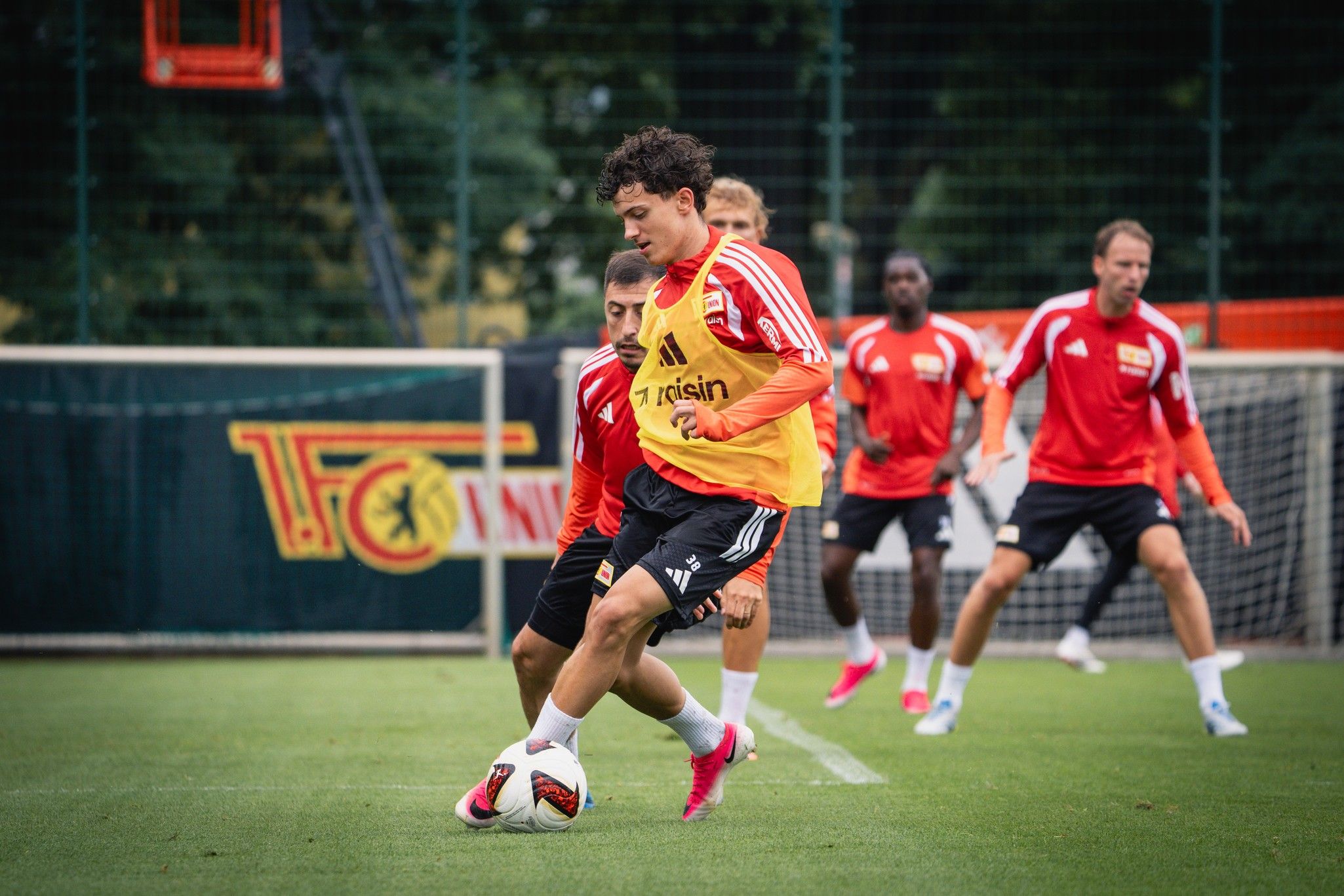 Fußballspieler üben im Training auf dem Feld, ein Spieler dribbelt den Ball, während andere positioniert sind.