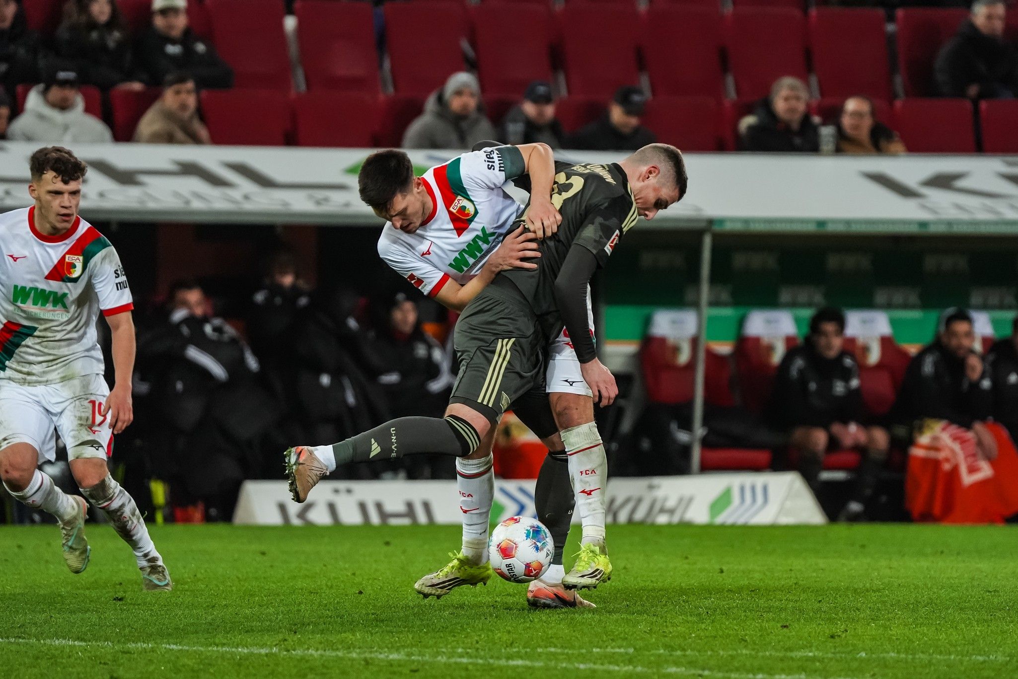 Ein Fußballspieler zieht einen anderen Spieler am Trikot während eines Spiels, im Hintergrund Zuschauer in einem Stadion.
