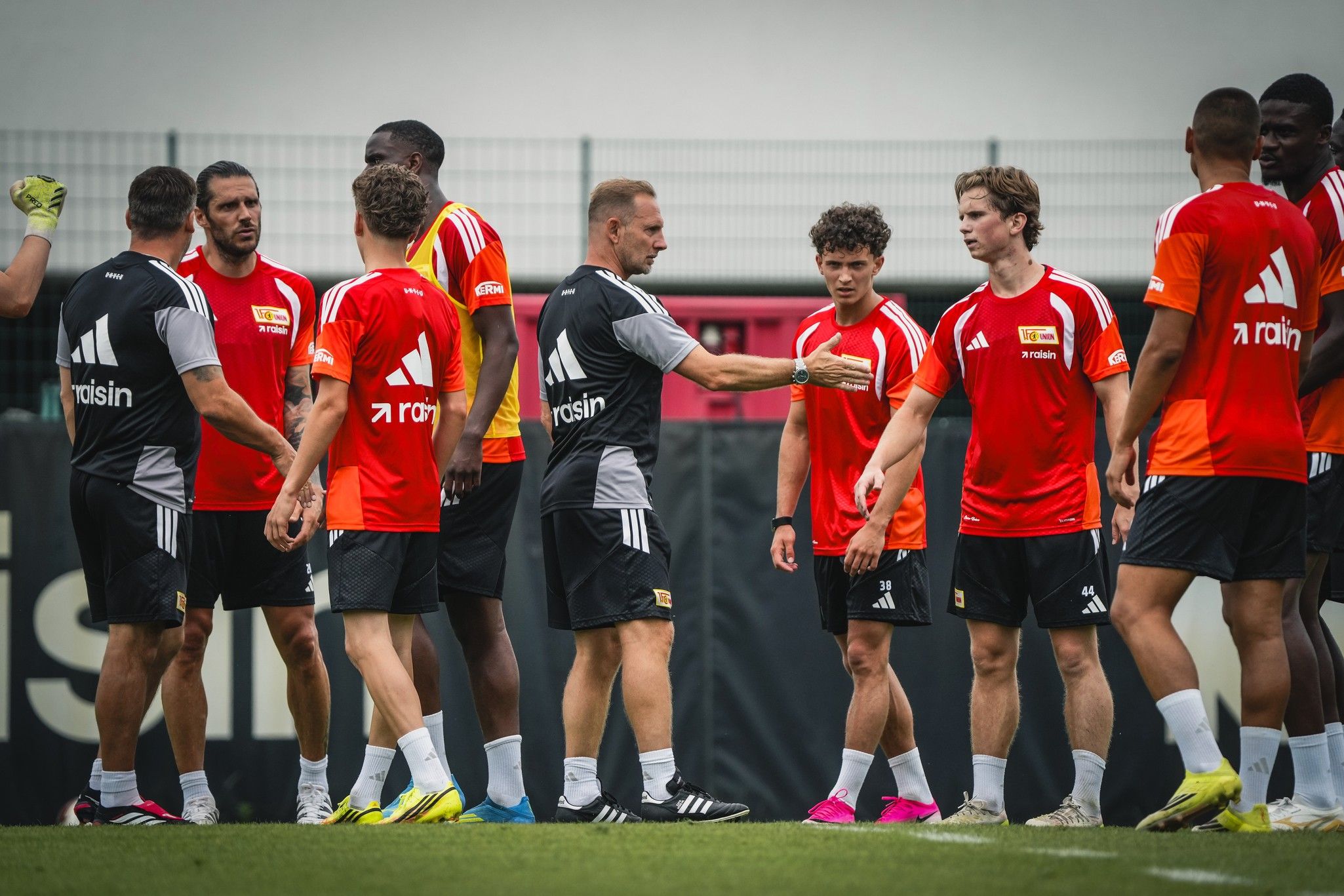 Ein Fußballtraining mit mehreren Spielern in roten Trikots und einem Trainer auf dem Platz.