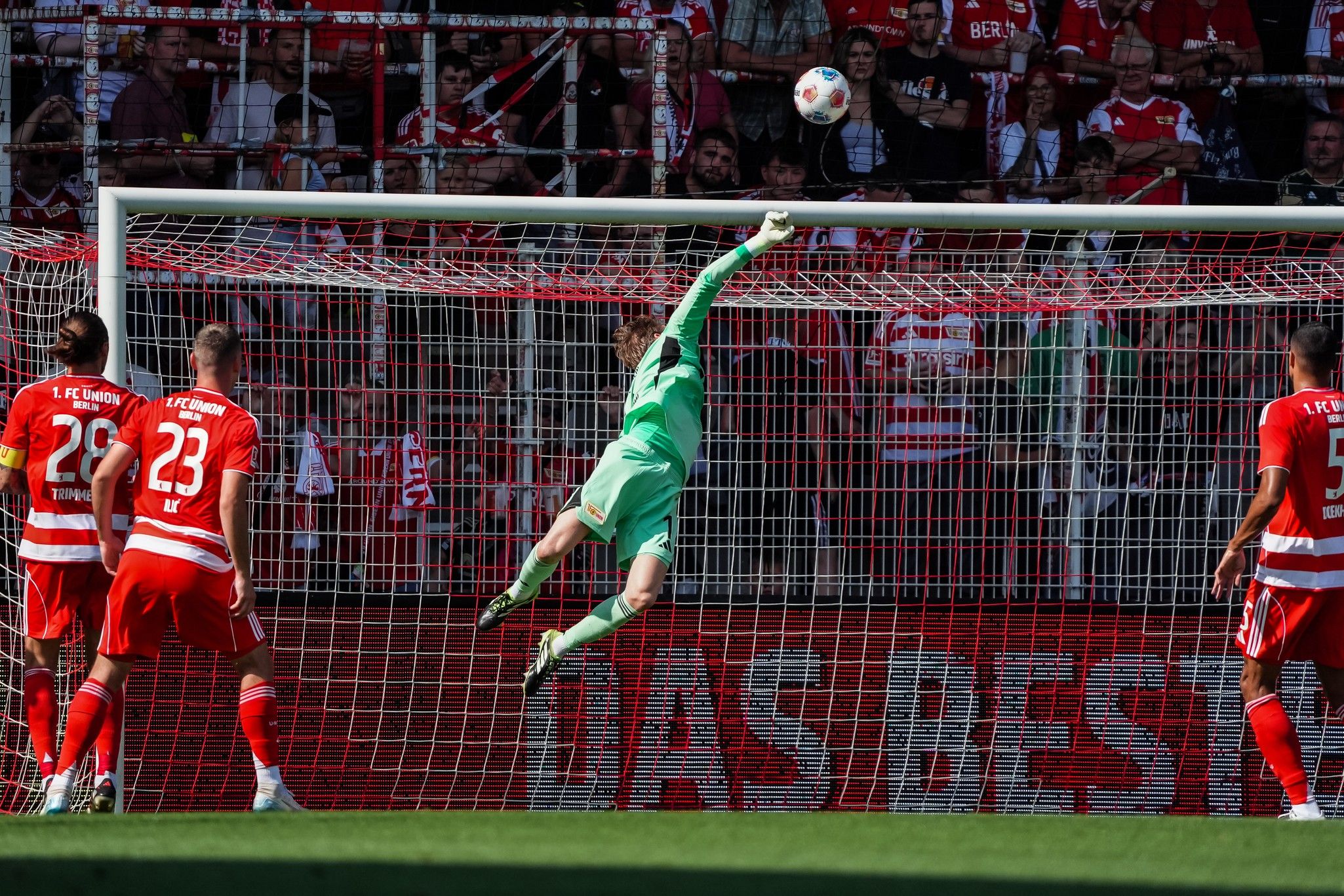 Torhüter springt, um den Ball während eines Fußballspiels zu retten. Zuschauer im Hintergrund.
