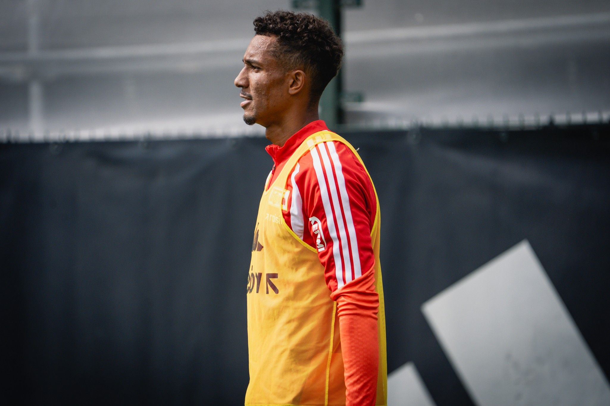 Ein Fußballspieler in Trainingskleidung steht seitlich und schaut nachdenklich.
