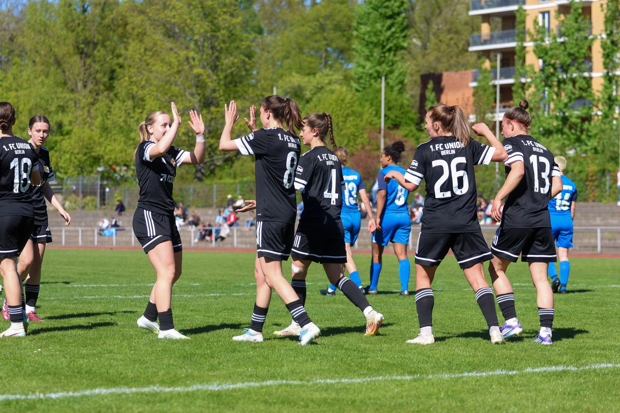 Spielerinnen einer Fußballmannschaft in schwarzen Trikots feieren einen Torerfolg auf dem Spielfeld.