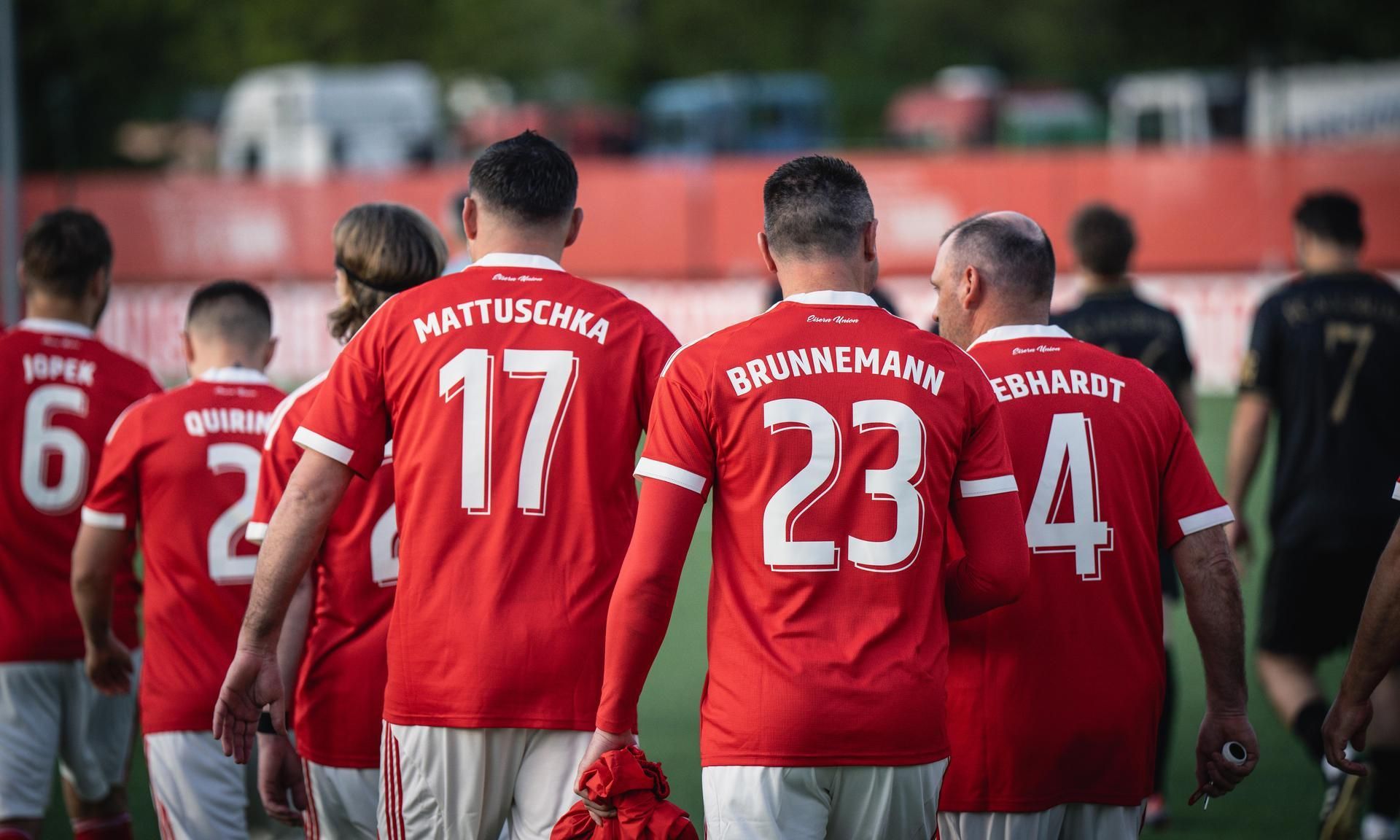 Spieler in roten Trikots mit Rückennummern gehen gemeinsam auf einem Fußballplatz.
