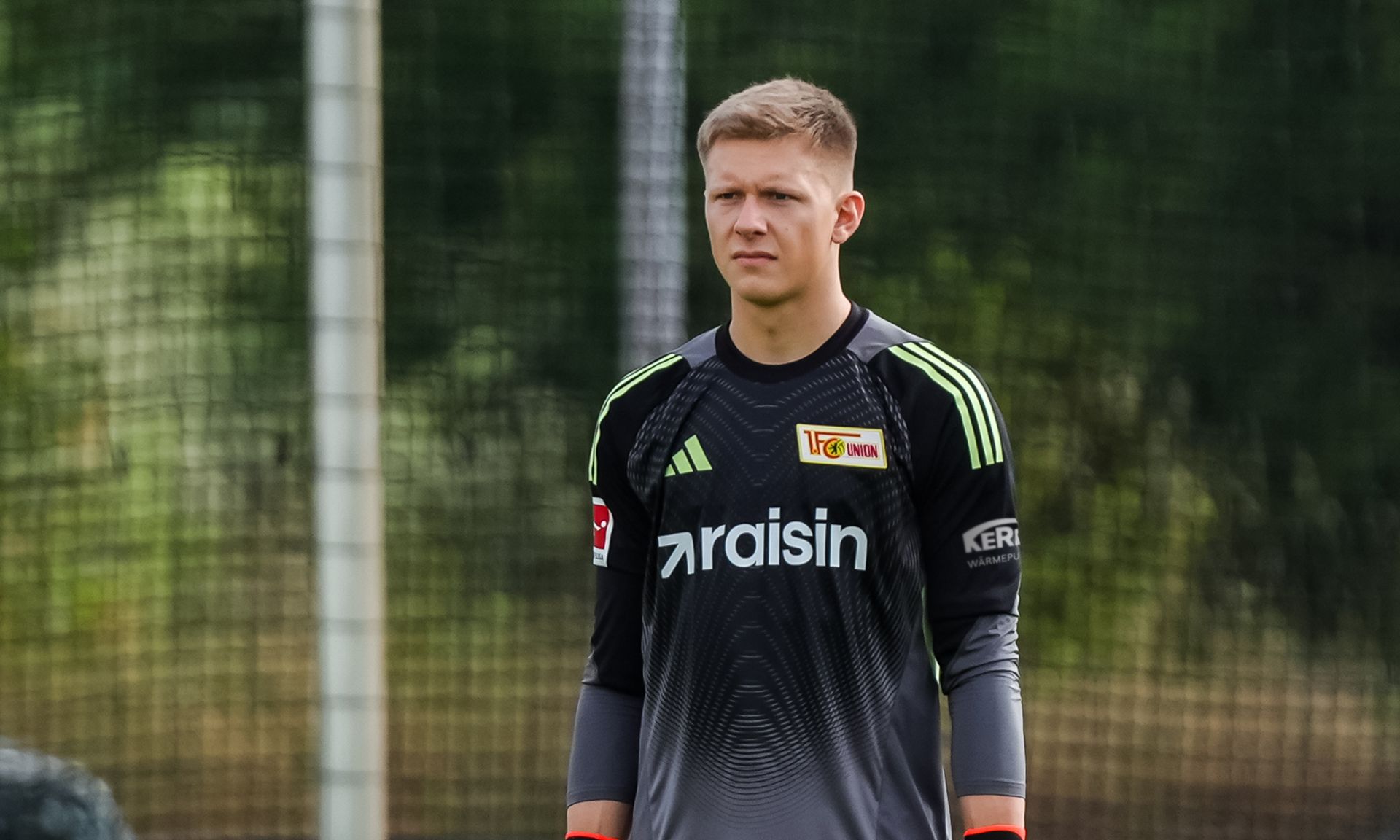 Ein Fußballtorwart steht in voller Ausrüstung auf dem Trainingsplatz und schaut nachdenklich in die Ferne.