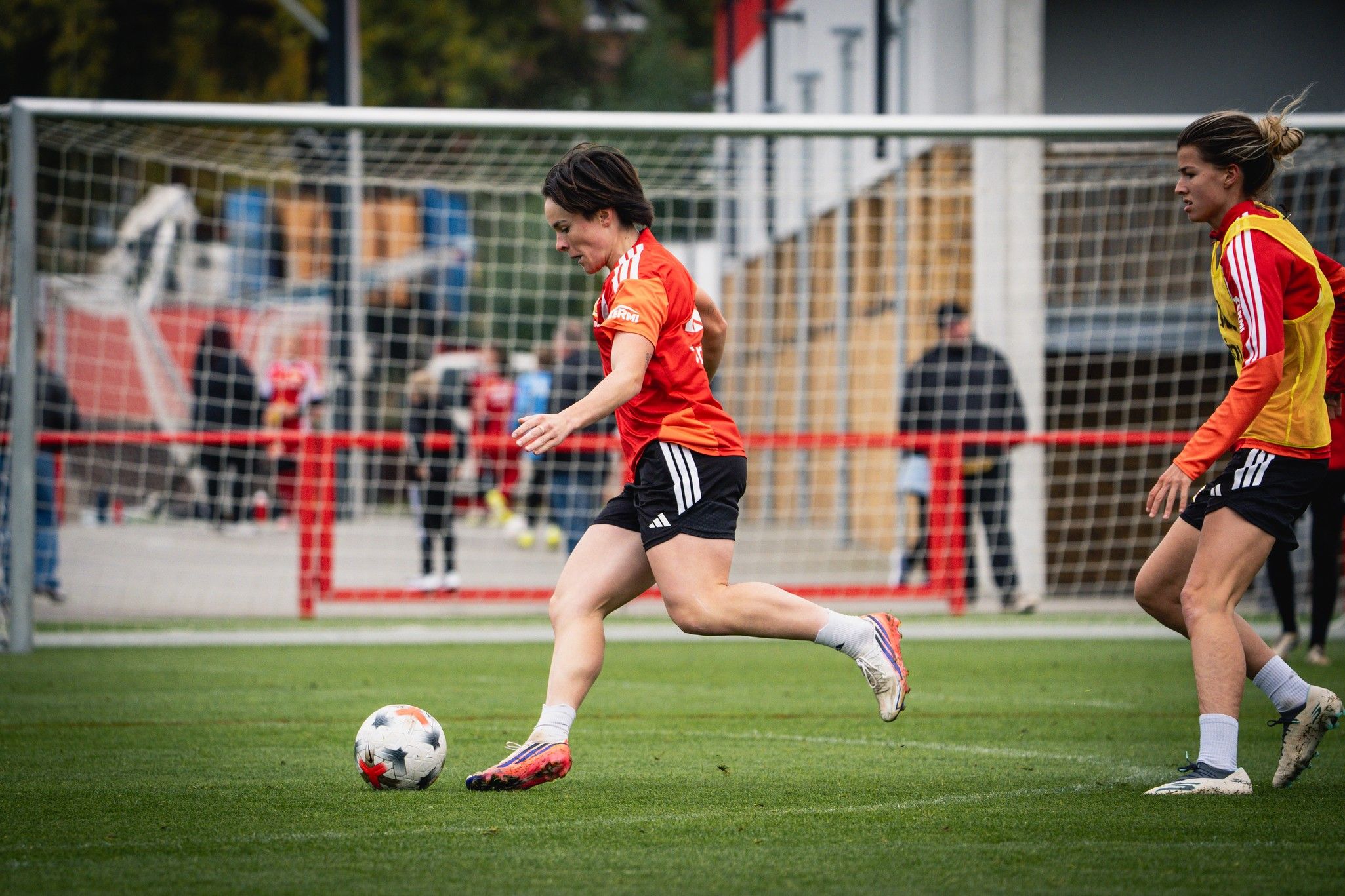 Zwei Frauen in Trikots spielen Fußball auf einem Trainingsplatz, während eine Spielerin den Ball dribbelt.