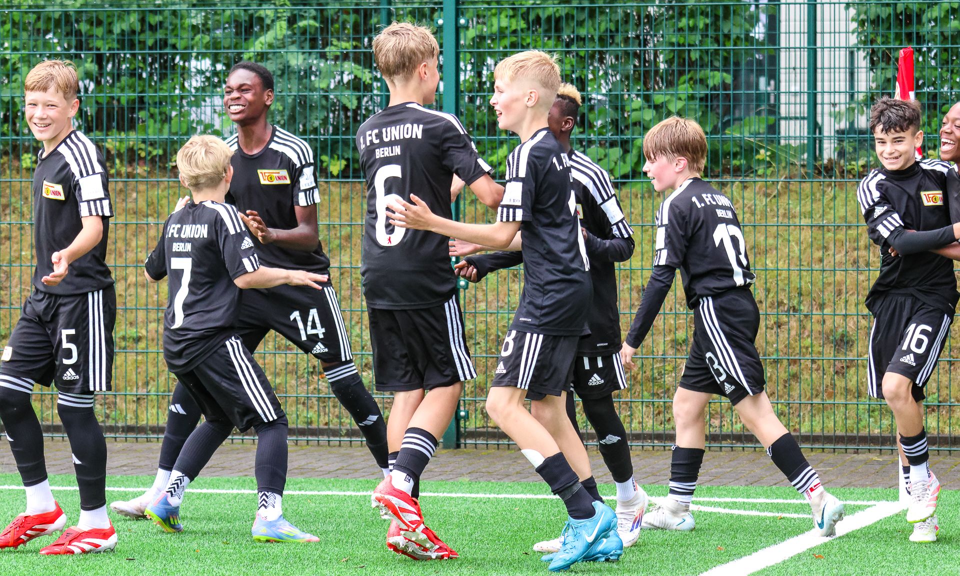 Gruppe von lächelnden Jungen in schwarzen Trikots, die auf einem Fußballplatz feiern und sich freuen.