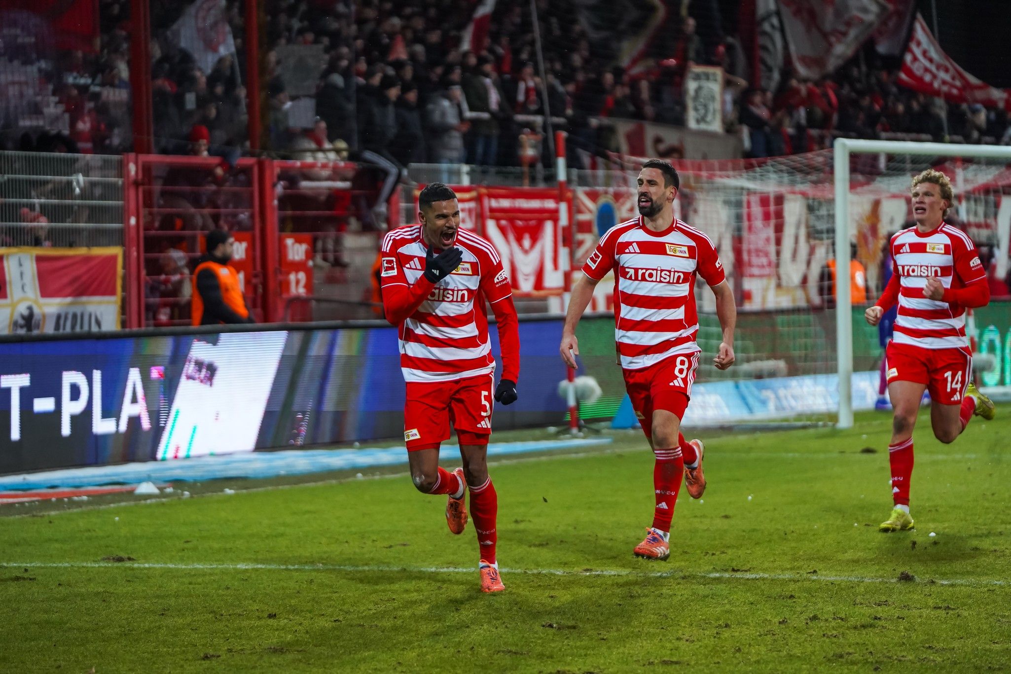 Spieler von Union Berlin feiern einen Torjubel im Stadion, Umgeben von Fans und traditionellen Stadionbanner.