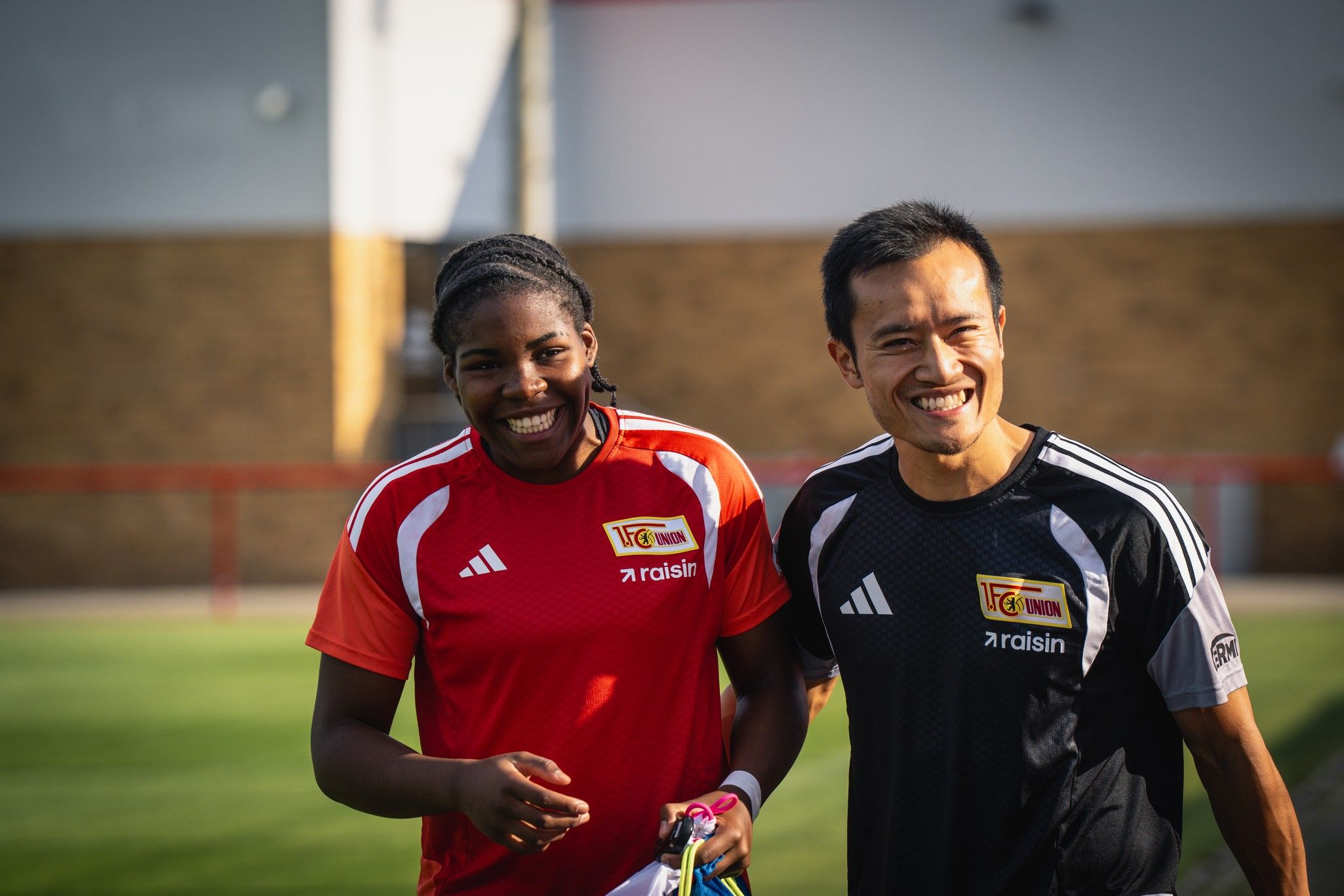 Zwei Sportler in Trainingskleidung lächeln lächelnd auf einem Sportplatz.