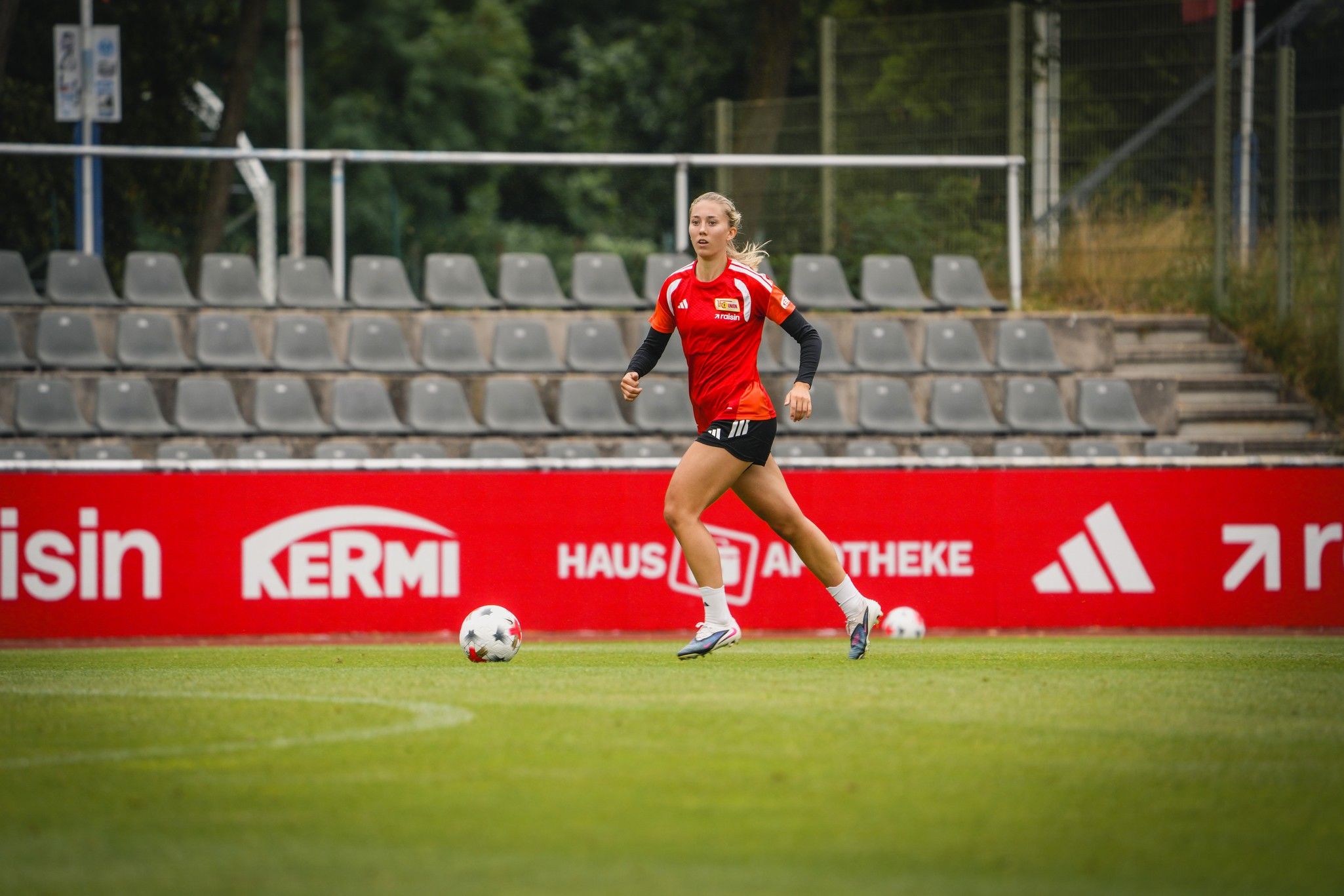 Eine Fußballspielerin in rotem Trainingsshirt läuft über das Spielfeld, während sie auf den Ball zusteuert.