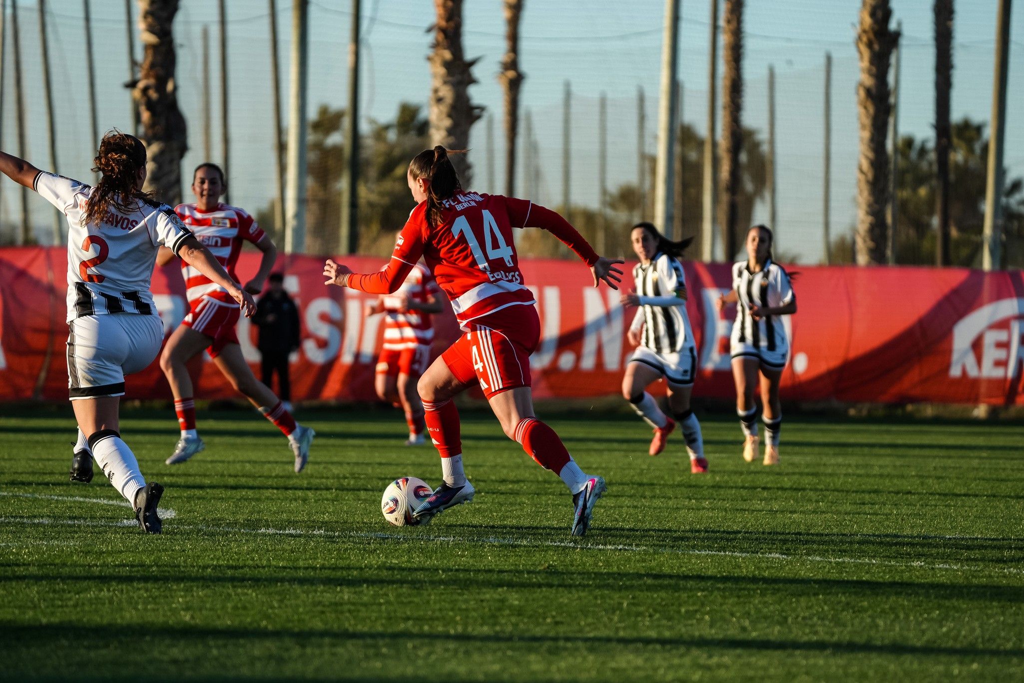 Eine Fußballspielszene mit mehreren Spielerinnen auf einem grünen Platz, während eine Spielerin mit der Nummer 44 den Ball dribbelt.