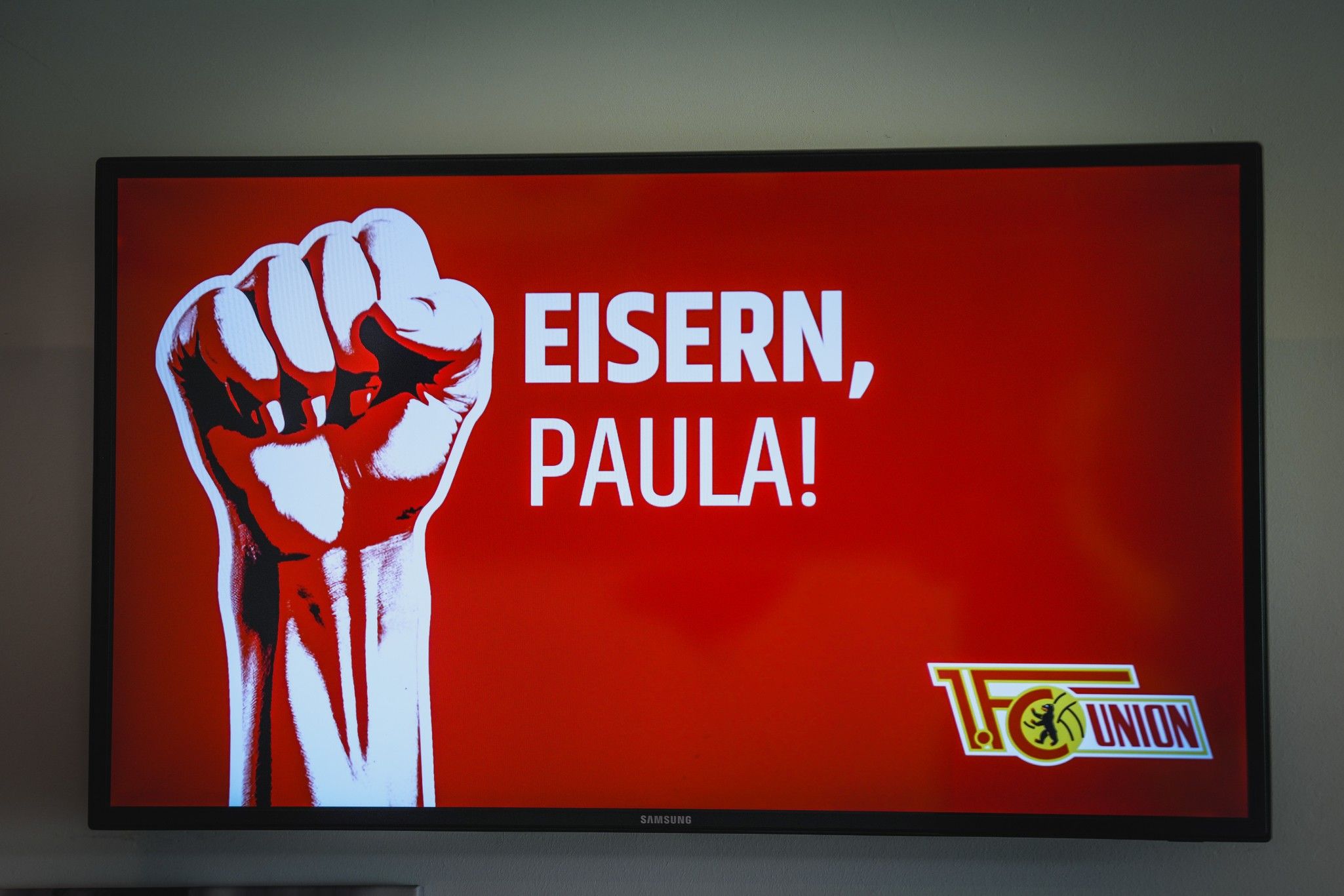 Ein Fernsehbildschirm mit der Grafik eines erhobenen Fists und dem Text "EISERN, PAULA!" auf rotem Hintergrund.