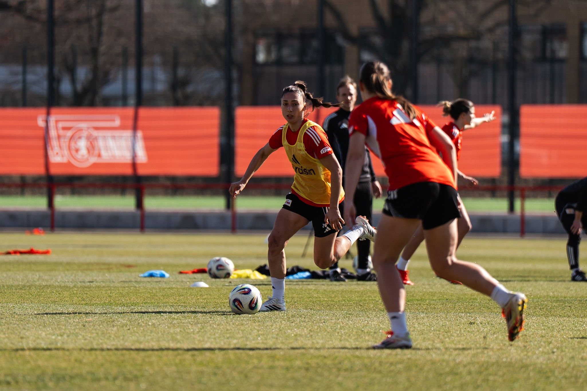 Eine Fußballspielerin läuft mit dem Ball, während andere Spielerinnen im Training hinter ihr agieren.