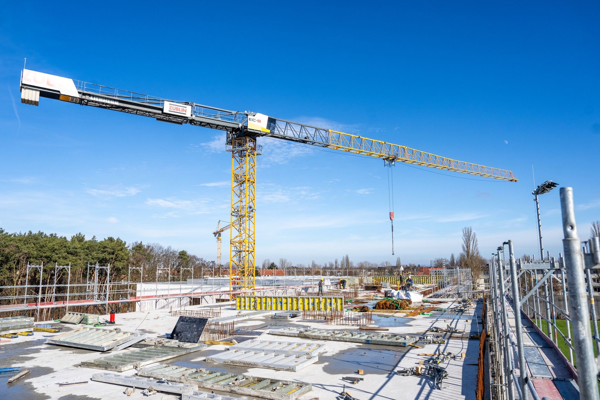 Bauplatz mit einem Kran über einer Baustelle und blauem Himmel im Hintergrund.