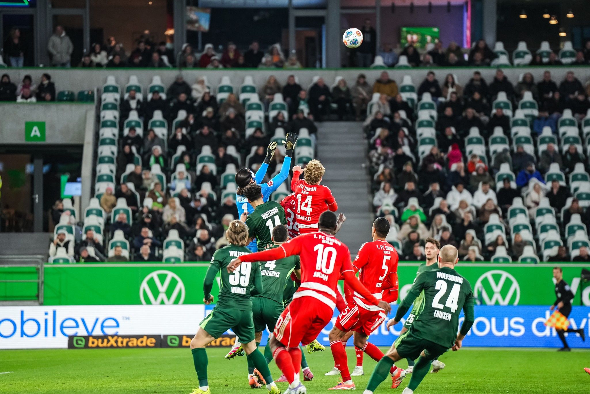 Torwart springt hoch, um den Ball während eines Fußballspiels zu fangen; Spieler beider Teams positionieren sich im Hintergrund.