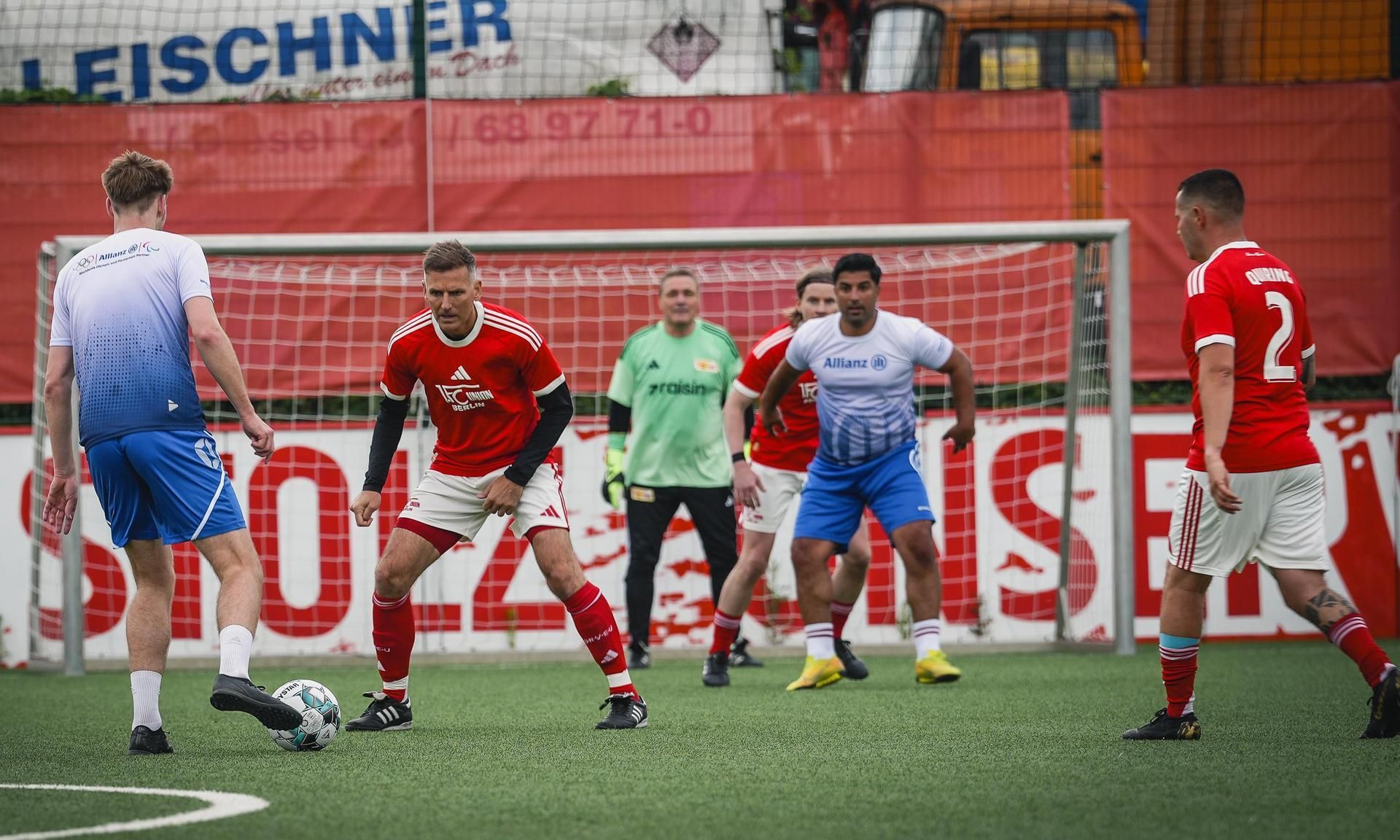 Zwei Gruppen von Fußballspielern auf einem Platz stehen sich gegenüber, während ein Spieler den Ball kontrolliert.
