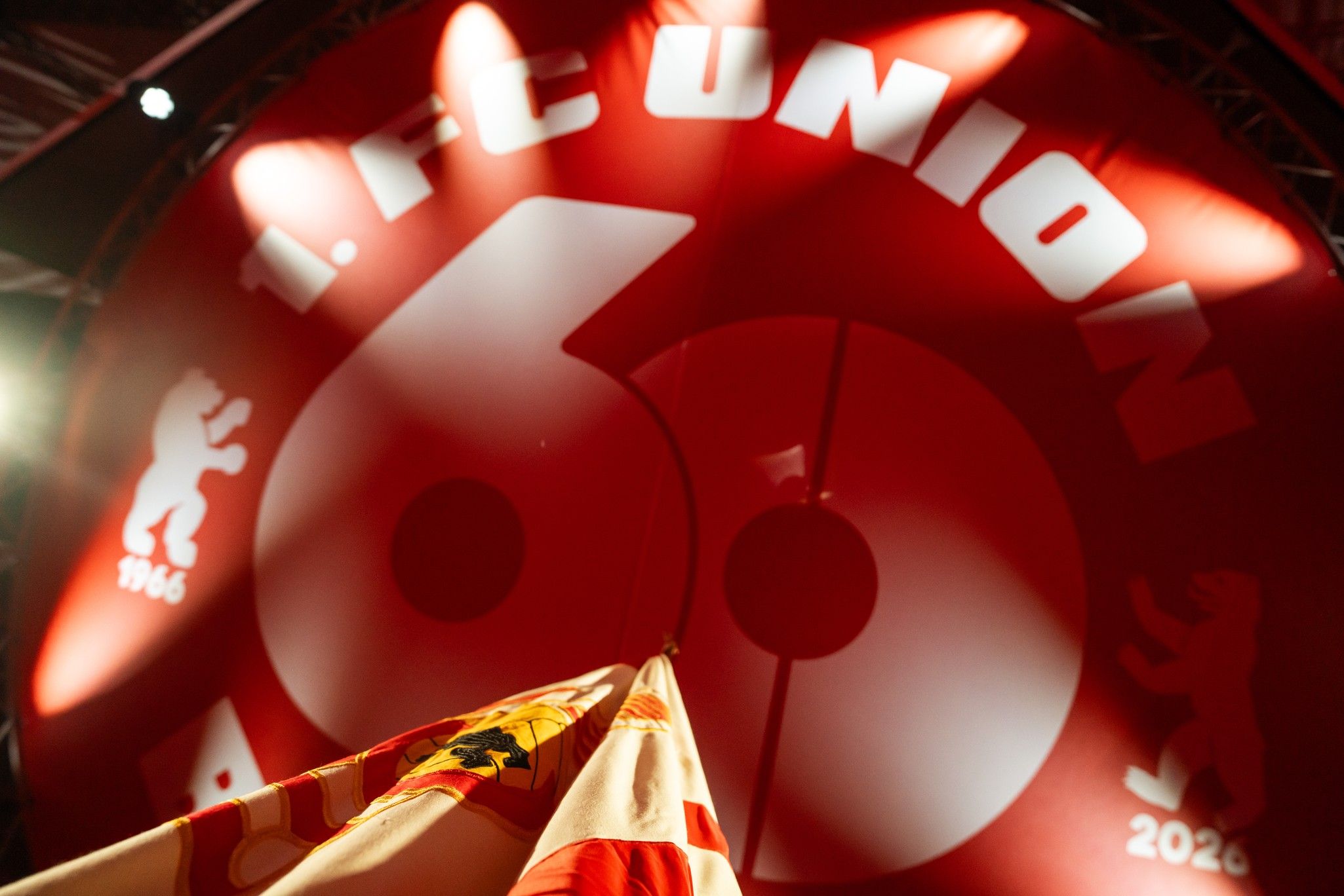 Ein rotes Banner mit der Aufschrift "1. FC UNION 60" und einem Bären. Im Vordergrund sind Fahnen zu sehen.